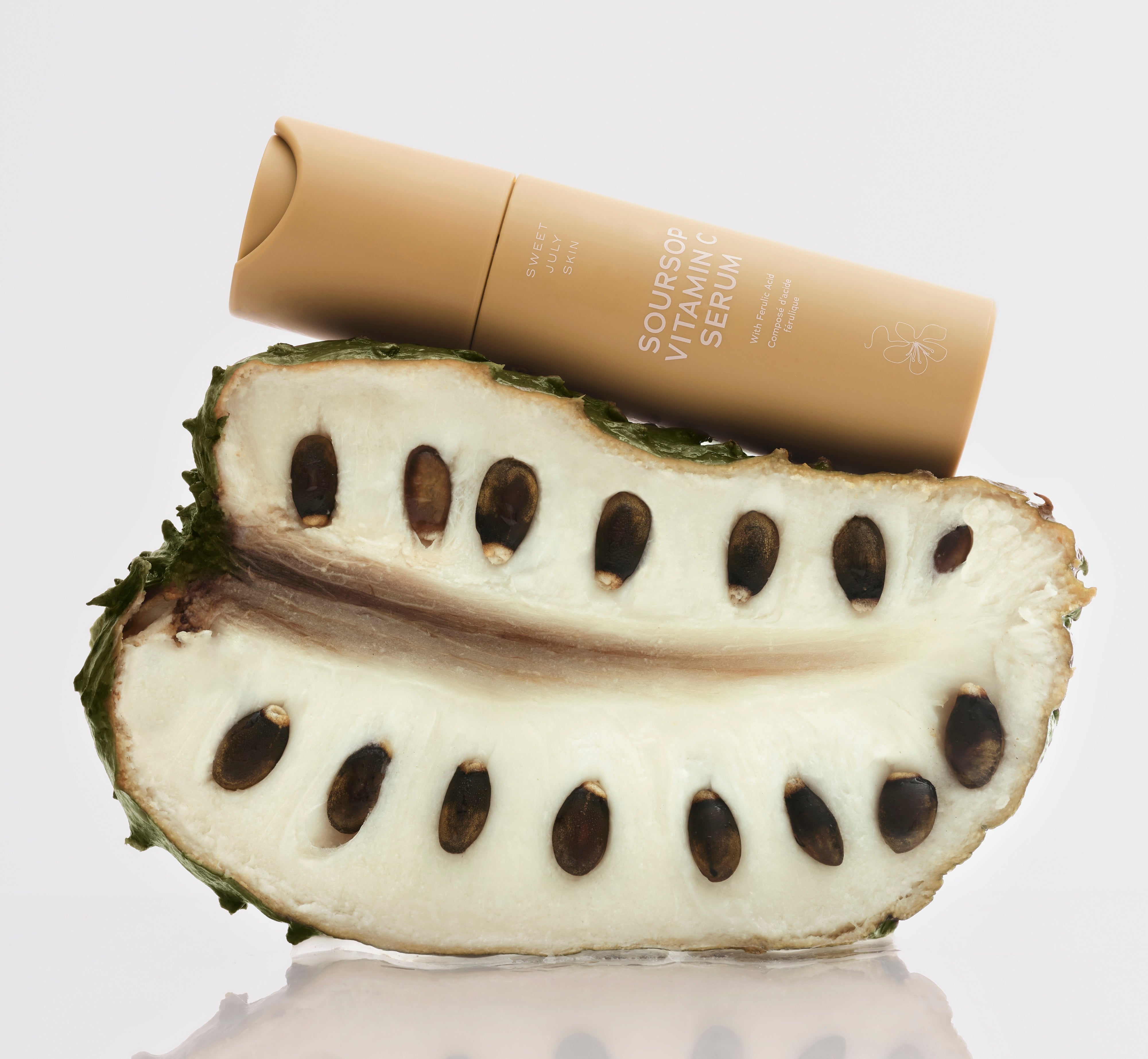Sweet July Skin Soursop Vitamin C Serum tube resting on halved soursop fruit
