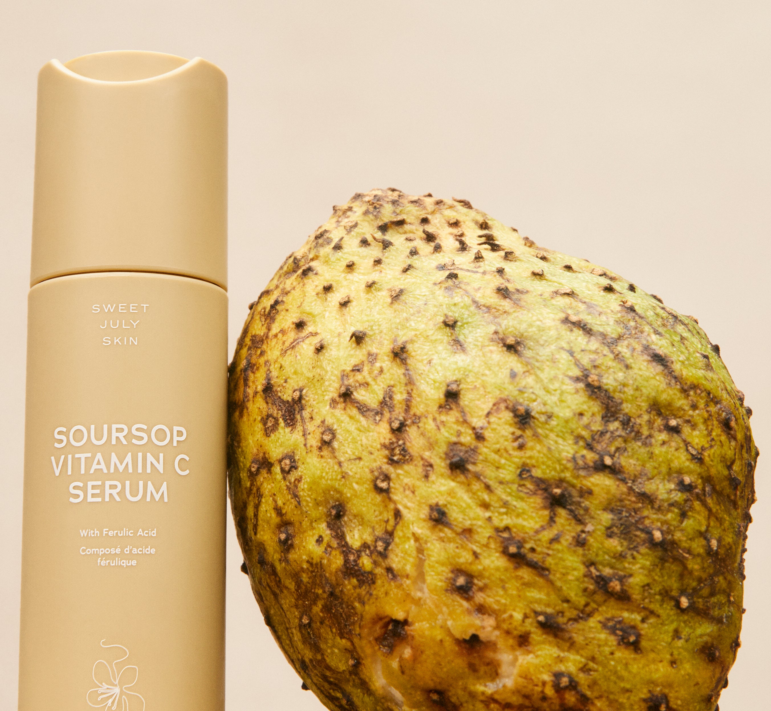 Soursop Vitamin C Serum bottle standing beside a whole green soursop fruit on a warm beige backdrop.