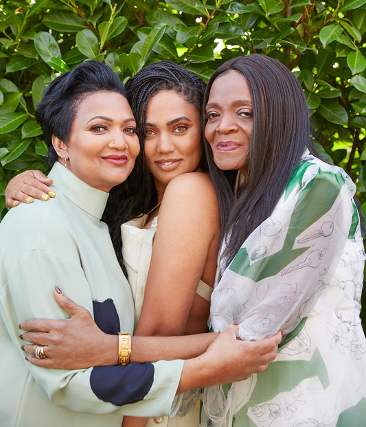 The image shows a group of women embracing outdoors. They appear happy and are dressed in wedding attire. It conveys a sense of friendship and love.