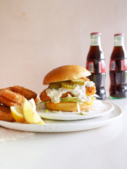 The image is a plate of American fast food, including a sandwich, hamburger, and a drink. It also features items like bread, baked goods, and fried food. The setting is indoor on a table.